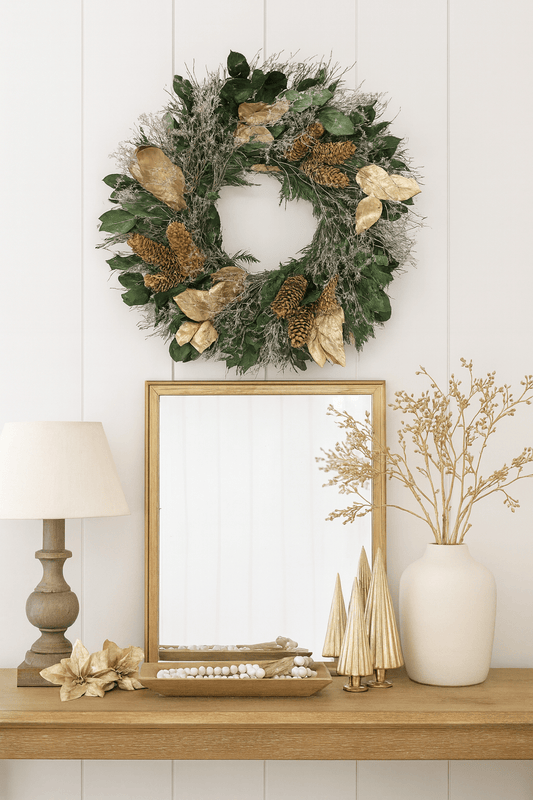 Christmas wreath with gold leaves and pinecones above a mirror on a desk