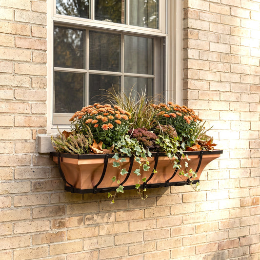 h potter brand window box with black metal brackets mounted on a beige brick wall beneath a window, filled with orange flowers and green foliage.
