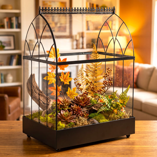 H Potter terrarium with a curved glass top, displayed on a wooden table in a cozy living room setting. The terrarium is filled with faux moss, succulents, autumn leaves, pinecones, and artificial ferns.