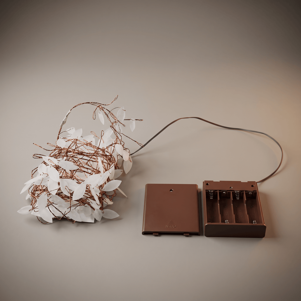 A battery-operated fairy light wire garland with white leaf-shaped bulbs, shown next to its brown plastic battery compartment and cover on a neutral beige background.