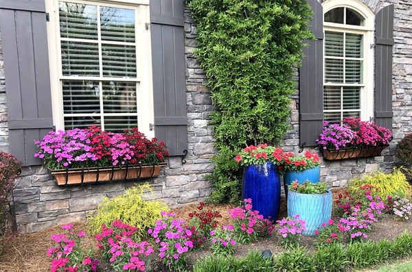 H Potter brand copper window boxes with flowers hanging on the outside of a house above a flower garden with planters