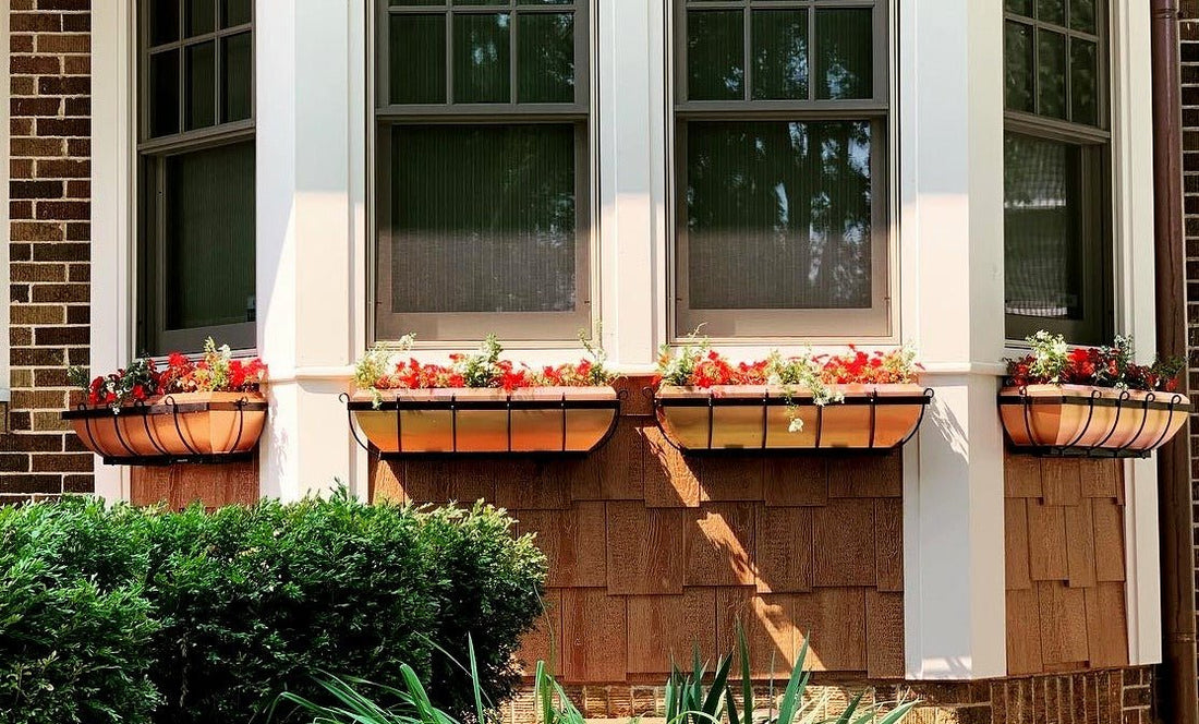 H Potter brand copper window box plant containers with flowers hanging on the outside of a house above a flower garden