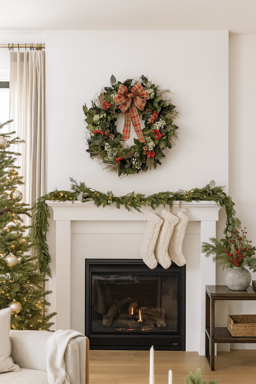 Decorative Christmas wreath with red plaid bow and red accents on a wall above a mantle in a living room 