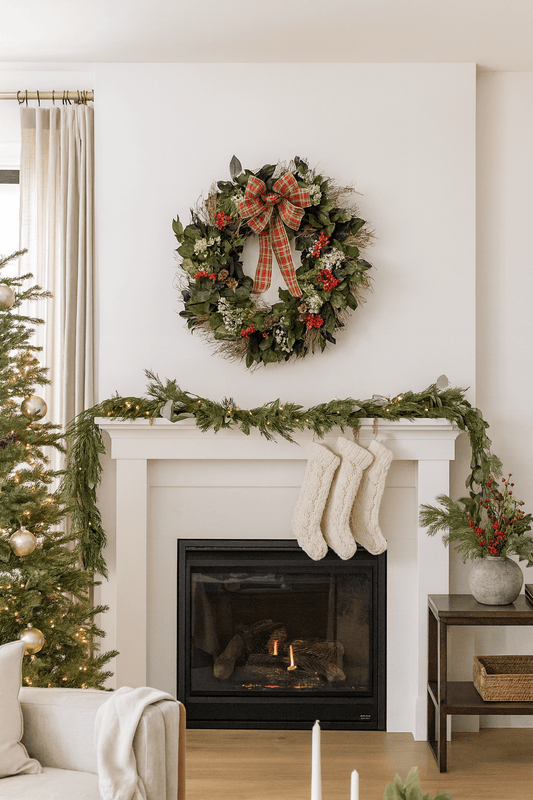 Decorative Christmas wreath with red plaid bow and red accents on a wall above a mantle in a living room 