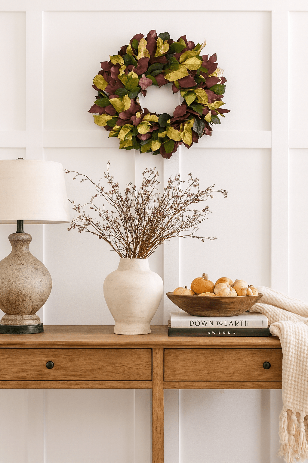 decorative wreath with red green and gold leaves on a white wall above a desk with white vase