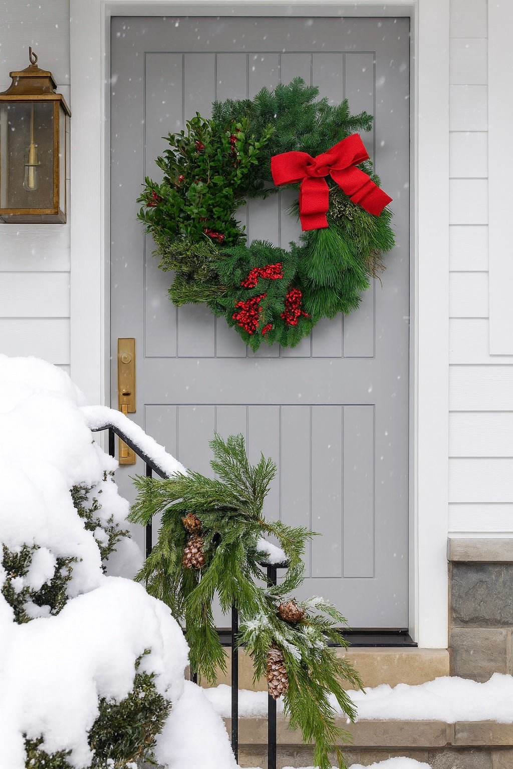 decorative christmas wreath with red berries and a red bow on a grey front door with snow