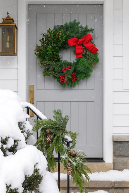 decorative christmas wreath with red berries and a red bow on a grey front door with snow