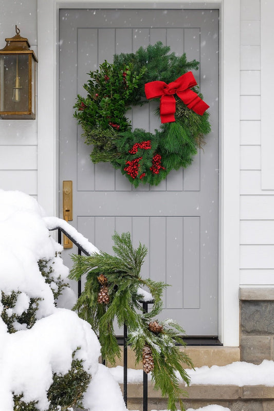 decorative christmas wreath with red berries and a red bow on a grey front door with snow