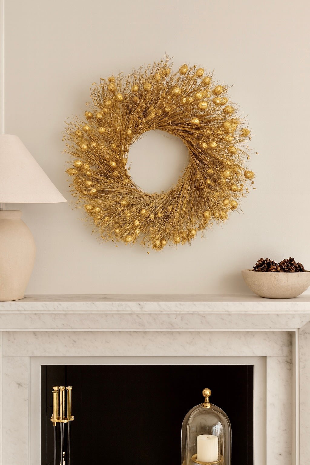 decorative gold christmas wreath above a mantle on a white wall