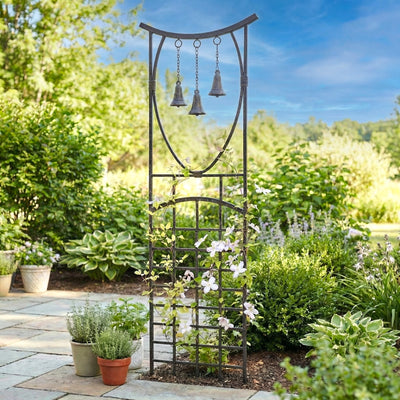 Decorative metal garden arch with hanging bells in a lush garden setting.