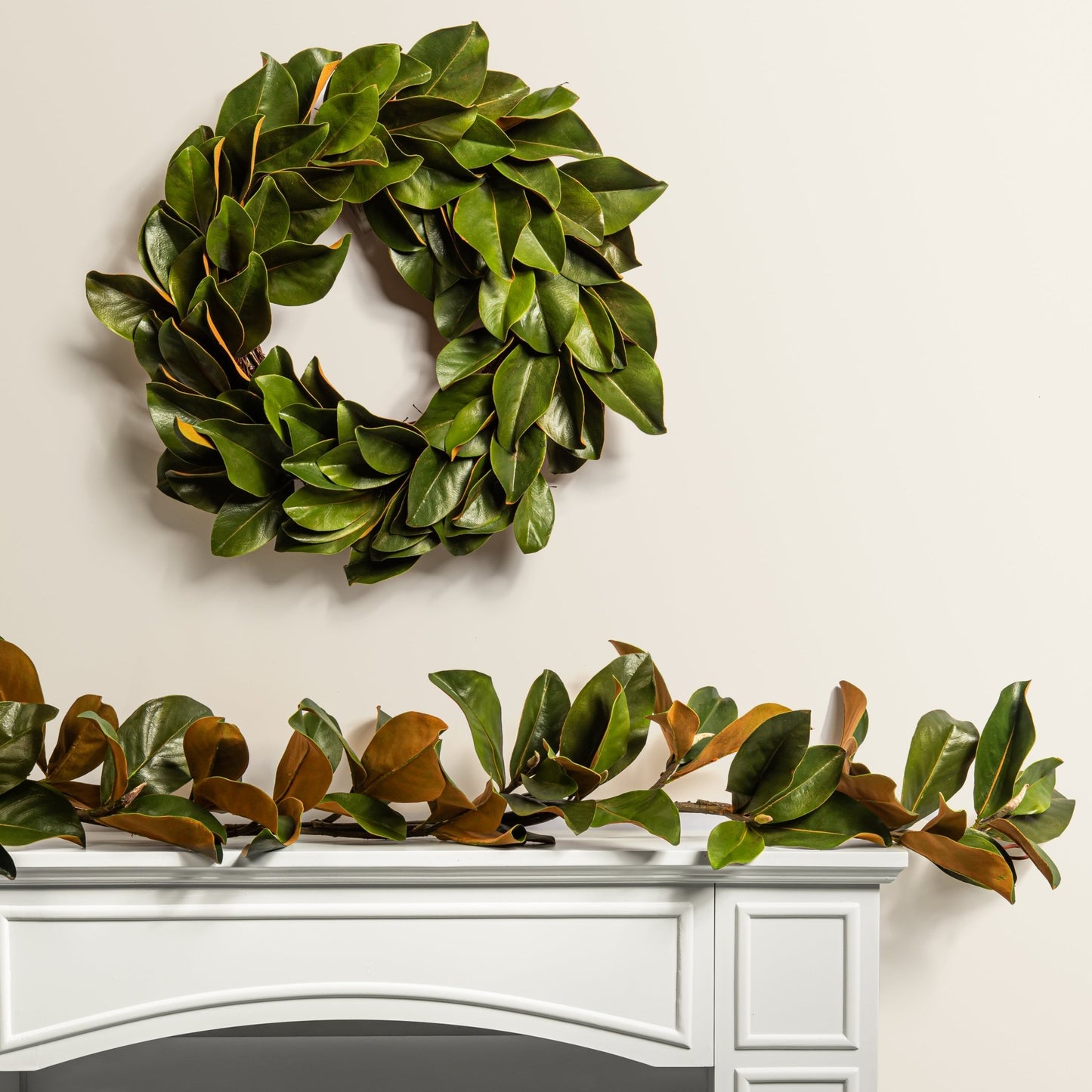 green leafy magnolia wreath with matching garland on a white mantel