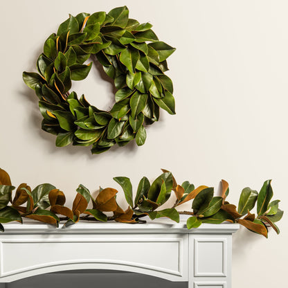 green leafy magnolia wreath with matching garland on a white mantel
