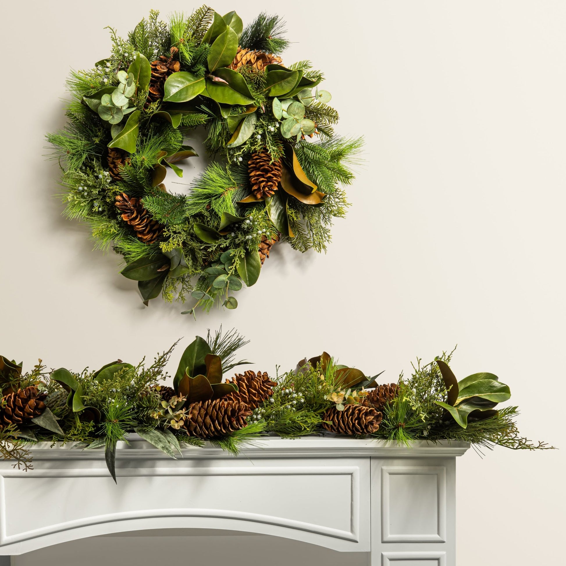 decorative pine wreath with pinecones above a matching wreath on a mantel
