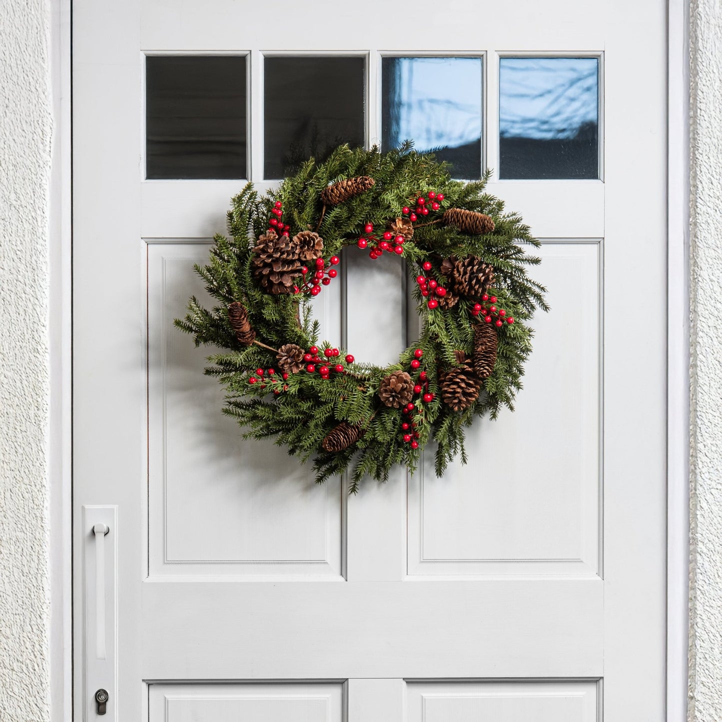 christmas wreath with red berries and pinecones on a white door