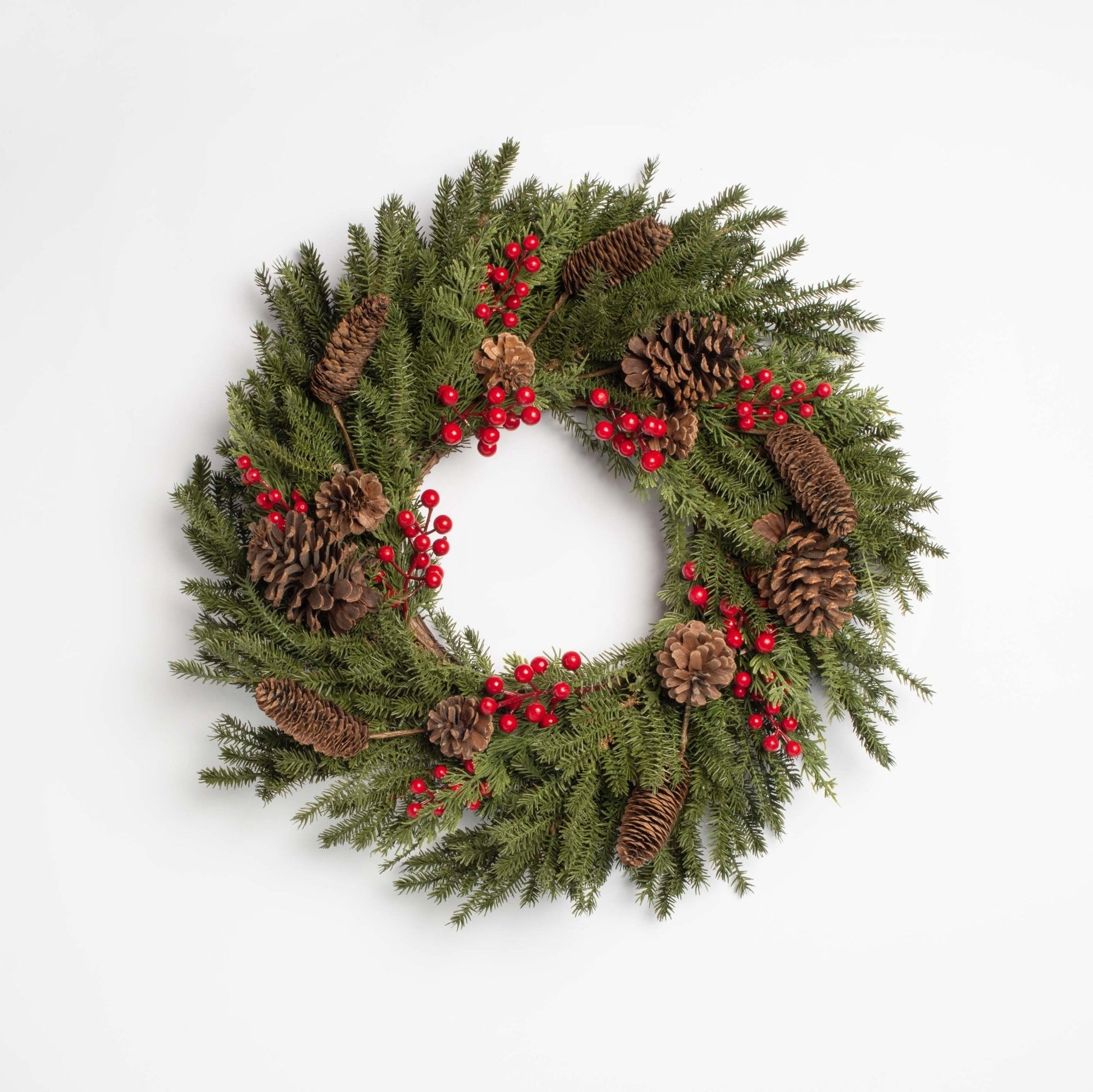 Christmas wreath with greenery, pinecones, and red berries on a white background