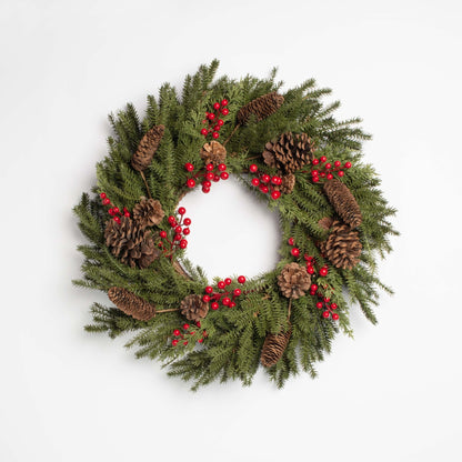 Christmas wreath with greenery, pinecones, and red berries on a white background