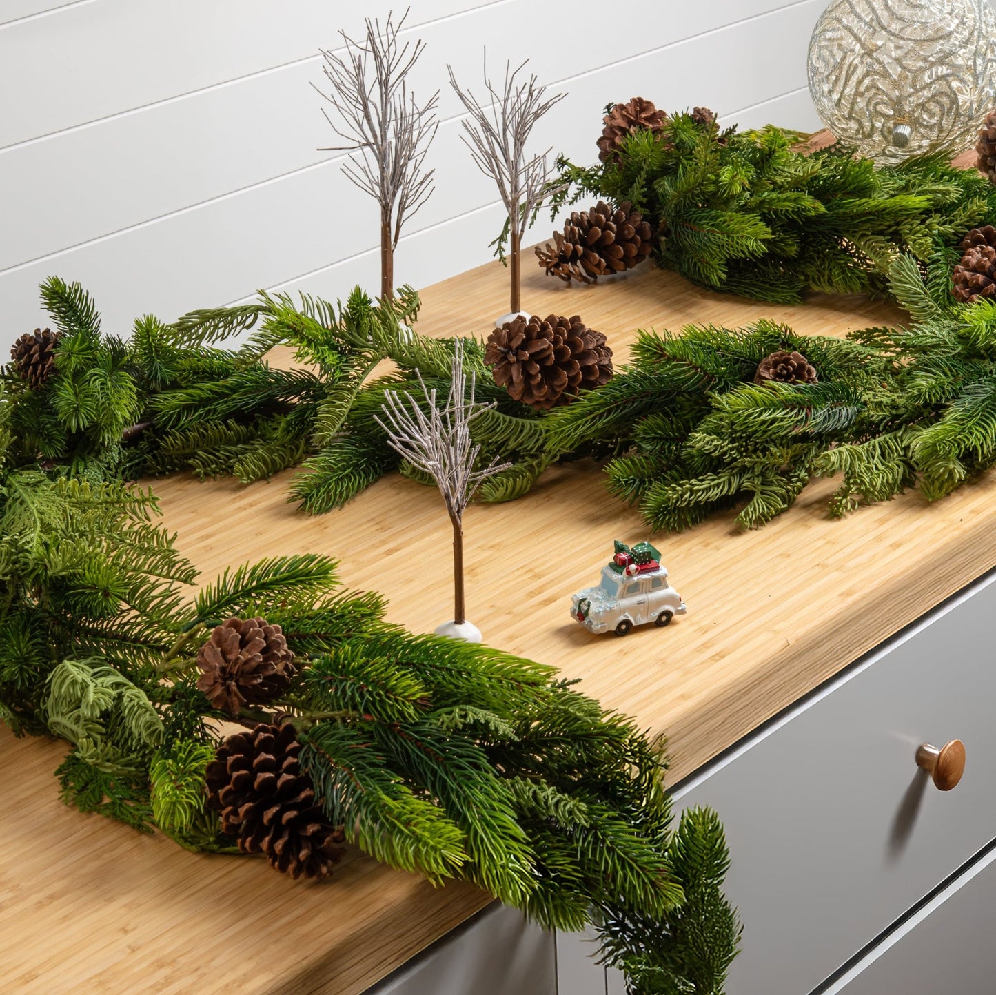 Decorative Christmas garland with pine cones and miniature trees on a wooden surface.