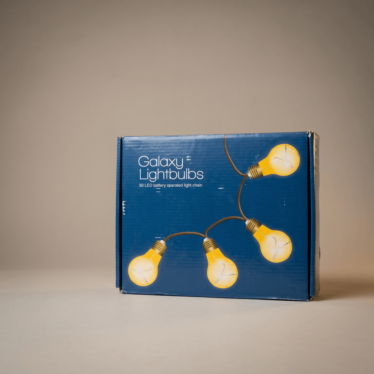 h potter blue retail box for Galaxy Lightbulbs, featuring illustrations of four glowing yellow lightbulbs on a string, photographed against a neutral beige background.