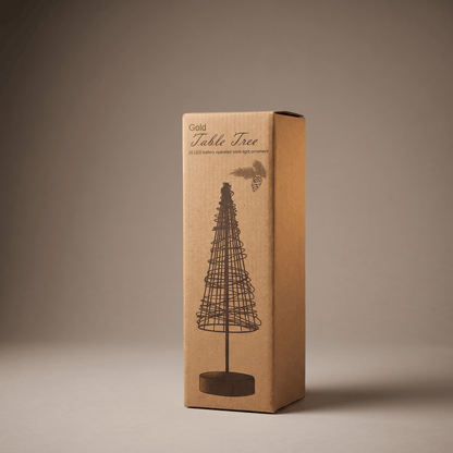 A tall rectangular cardboard box for a gold table tree, shown standing upright on a neutral warm gray studio background. The box is kraft brown with a printed black line drawing of the tree and the words 'Gold Table Tree' near the top.