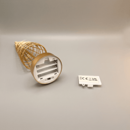 A gold wire tree with its white battery compartment visible and a small white CE mark card placed beside it on a neutral gray background.