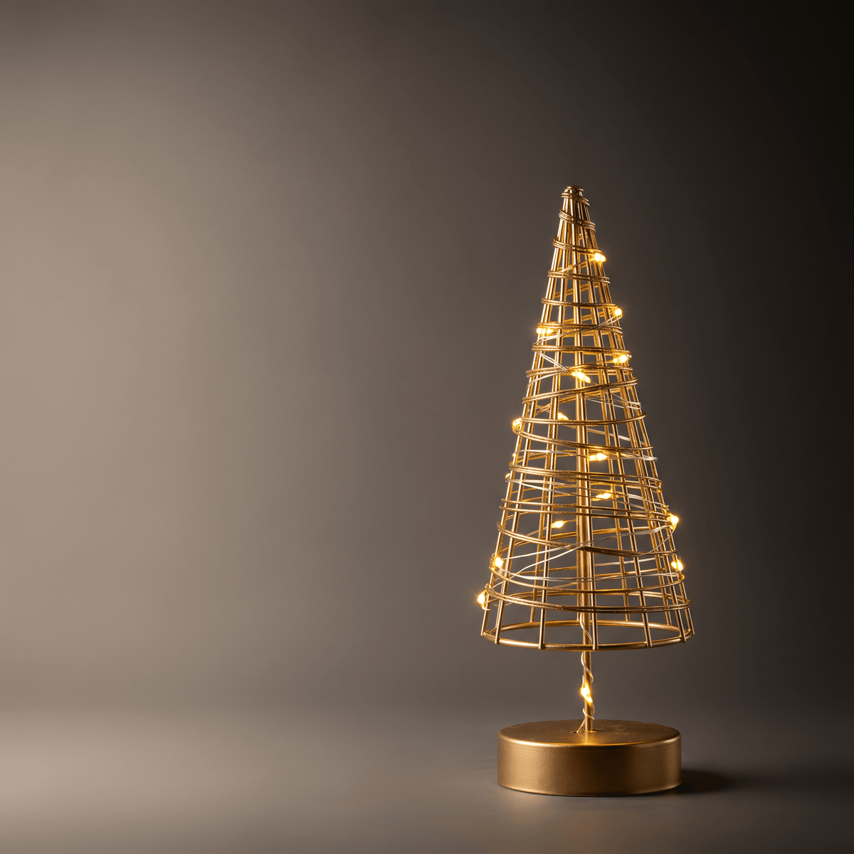 A gold wireframe cone-shaped decorative tree with warm glowing lights and a round gold base, photographed against a dark gray studio background.