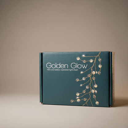 A dark teal product box for 'Golden Glow' 100 LED battery operated light chain, featuring a graphic of glowing pearlescent branches on a warm beige background.