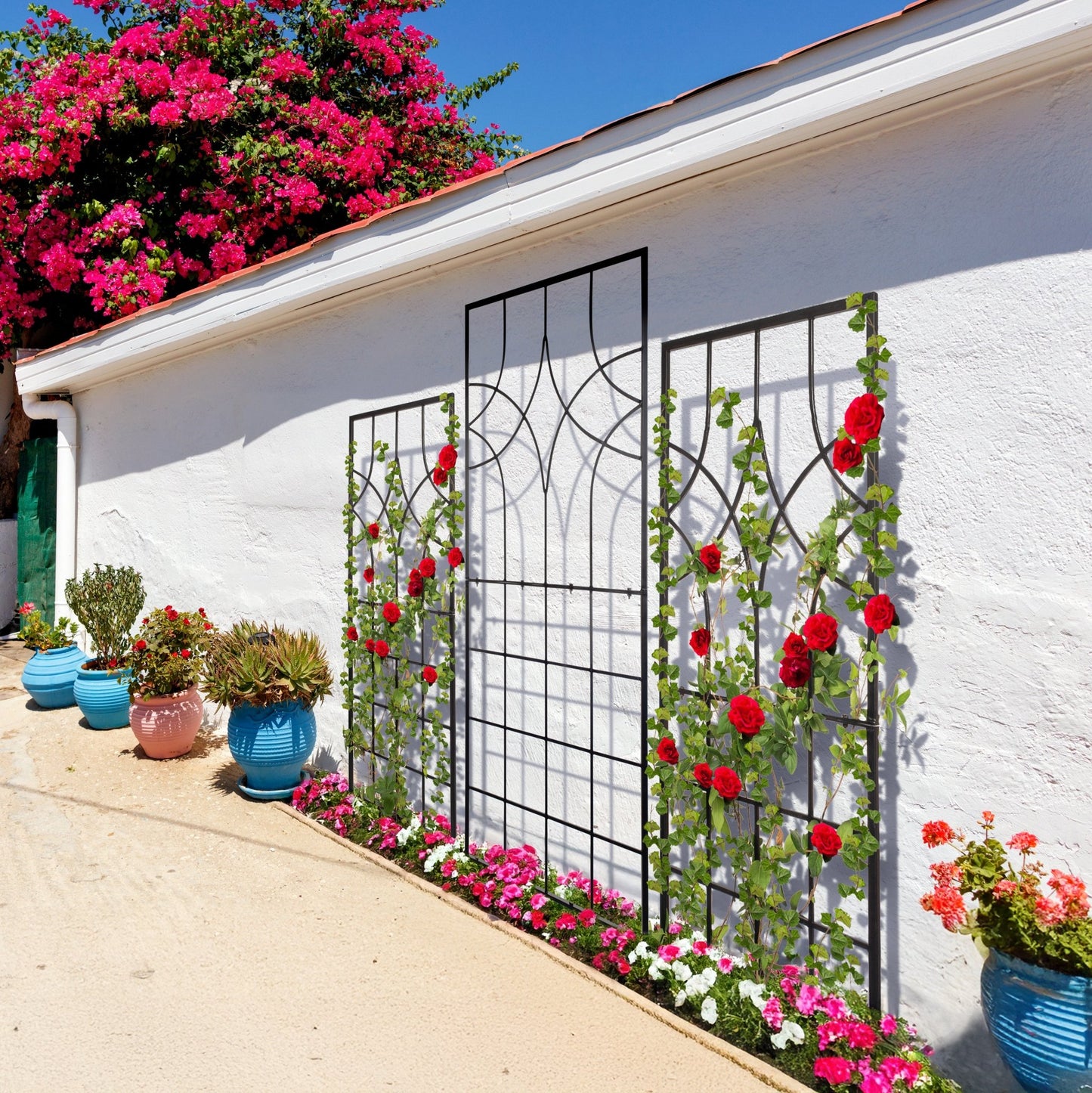 White wall with decorative metal trellises and climbing plants, surrounded by potted plants and flowers.