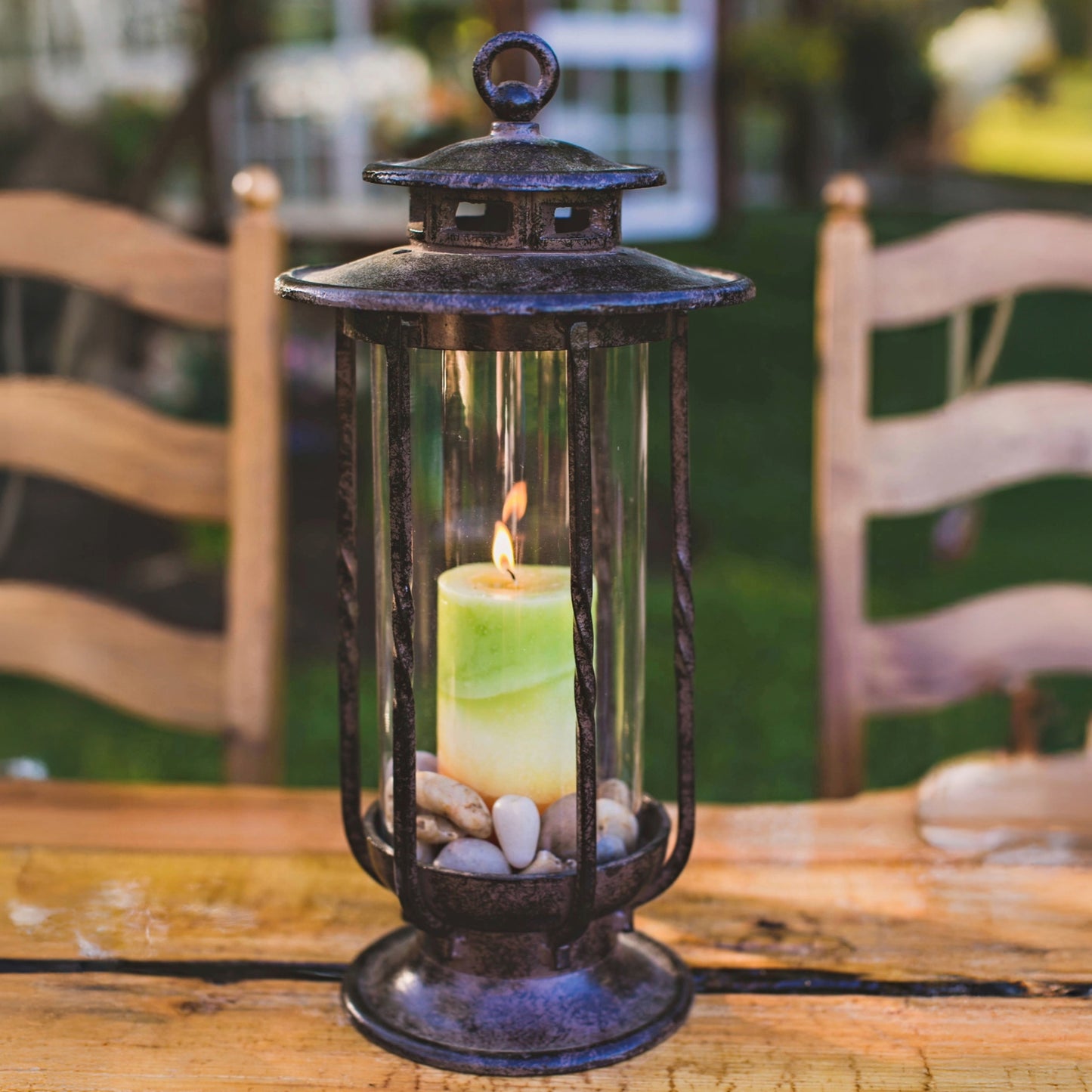 H Potter cast iron hurricane lantern with clear glass and lit candle displayed on an outdoor table for patio or garden décor.