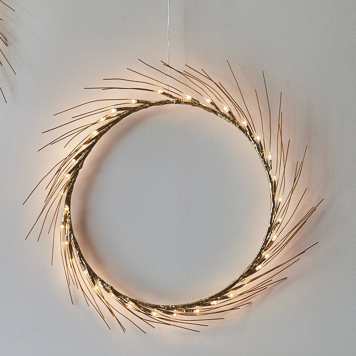 H Potter Celeste lighted wreath, small, warm LED lights on slender gold-toned spokes against a white wall