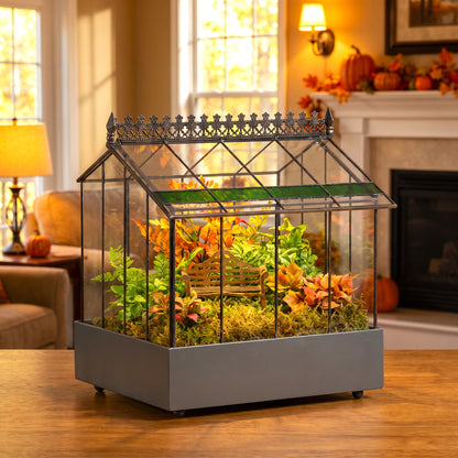 h potter brand terrarium with a gray metal base filled with faux moss, greenery, and autumn leaves, displayed on a wooden table in a cozy living room setting.