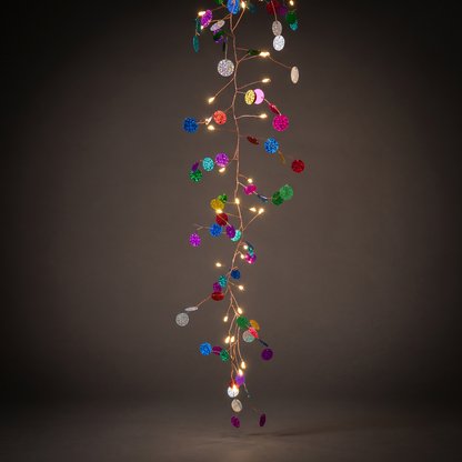 h potter vertical string of decorative fairy lights with small warm white bulbs and many colorful round sequin-like ornaments in blue, green, pink, purple, orange, and silver, set against a dark gray studio background.