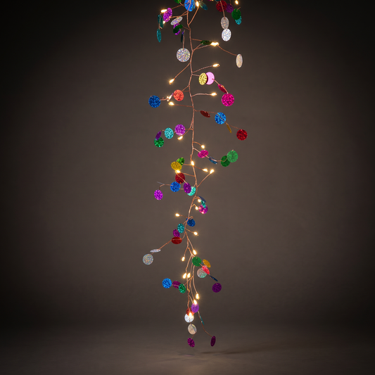 h potter vertical string of decorative fairy lights with small warm white bulbs and many colorful round sequin-like ornaments in blue, green, pink, purple, orange, and silver, set against a dark gray studio background.