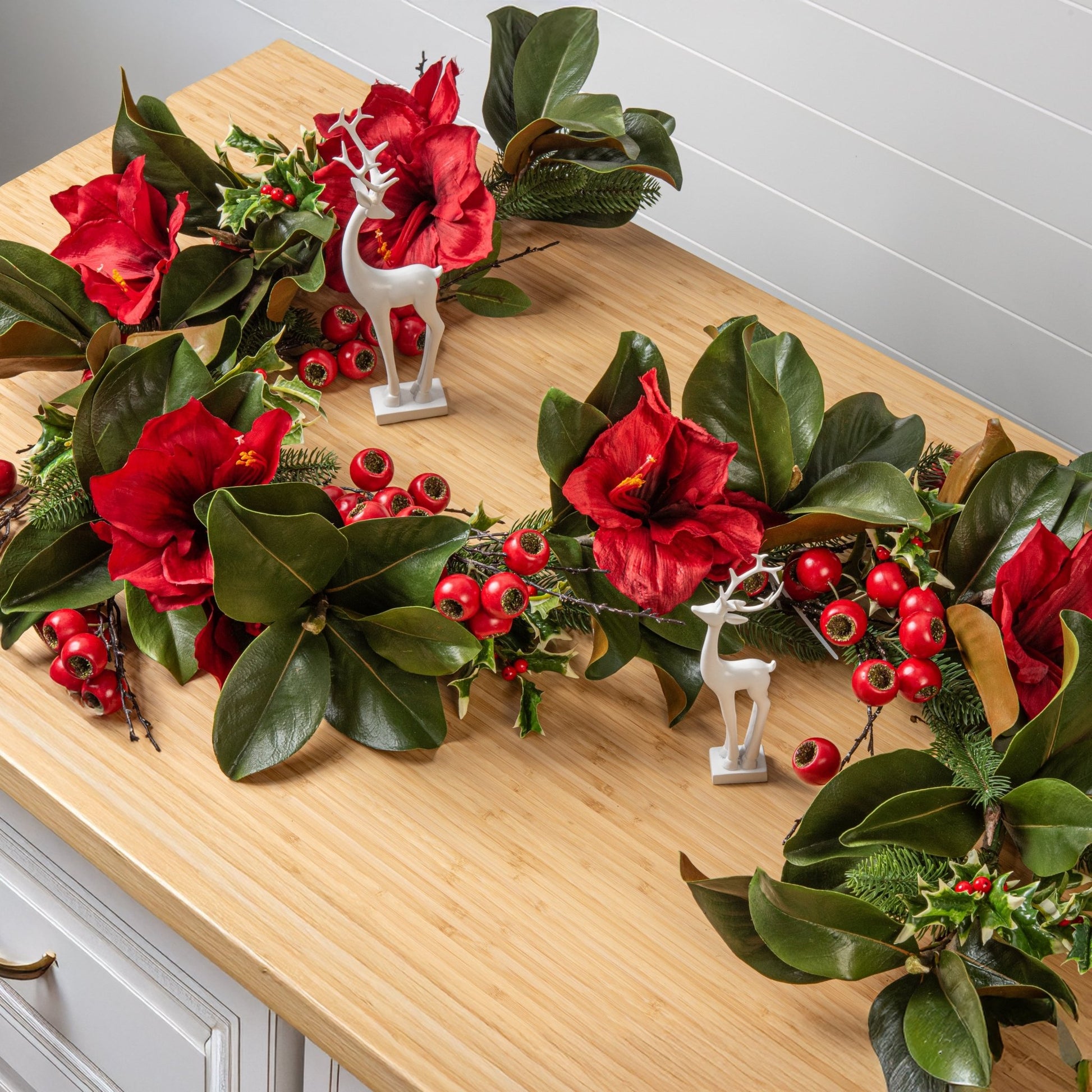 Decorative wreath with red flowers and green leaves on a wooden surface.