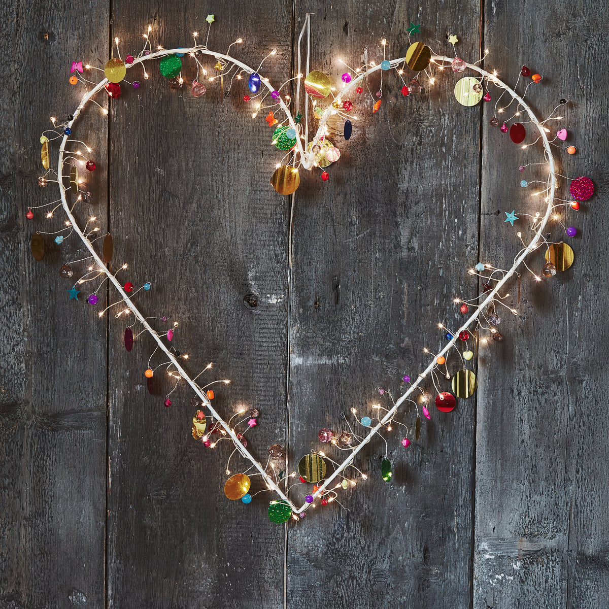Heart Enchanted Jewel lighted wreath glowing against a pale grey wall, beads sparkling in the warm light
