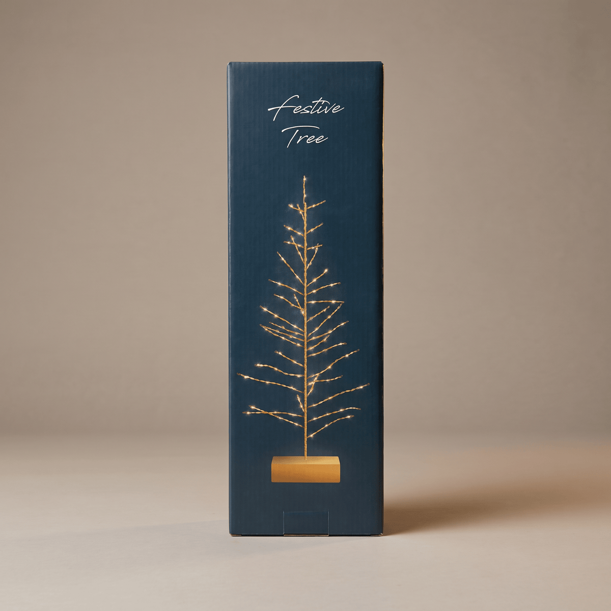 h potter tall, narrow dark blue-green gift box with a gold wire tree illustration and the words 'Festive Tree' on the front, photographed against a warm beige studio background.