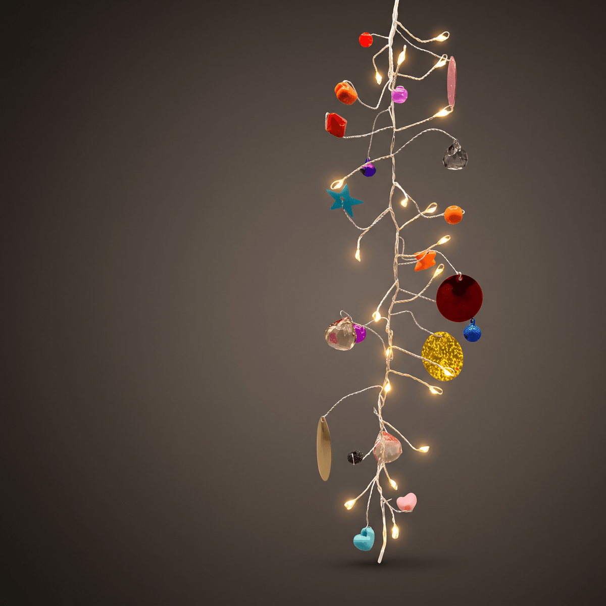 h potter folklore hanging string of decorative fairy lights with warm white bulbs and assorted colorful ornaments, including red, orange, pink, blue, yellow, and metallic pieces, set against a dark gray gradient background.