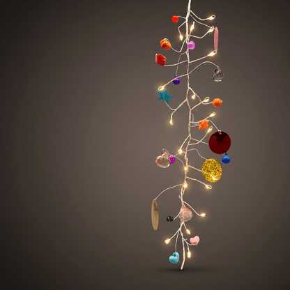 h potter folklore hanging string of decorative fairy lights with warm white bulbs and assorted colorful ornaments, including red, orange, pink, blue, yellow, and metallic pieces, set against a dark gray gradient background.