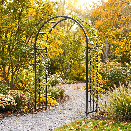 h potter black metal garden archway with climbing ivy and white flowers, situated on a gravel path in a lush autumn garden with yellow and orange foliage.