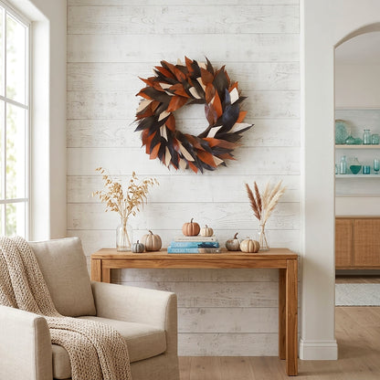 h potter brand decorative autumn leaf wreath in warm brown, rust, and cream tones hangs on a white shiplap wall above a wooden console table styled with pumpkins, books, and dried grasses in a bright living room.