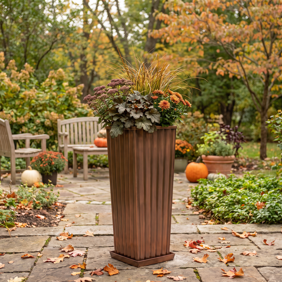 h potter brand tall, fluted rectangular planter in a warm antique copper finish, filled with ornamental grass and fall flowers, set on a stone patio in an autumn garden.