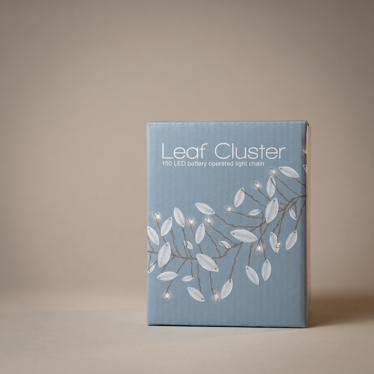 A rectangular product box for a 'Leaf Cluster' 150 LED battery operated light chain, featuring a light blue cover with white leaf illustrations and brown branch details, set against a neutral beige background.