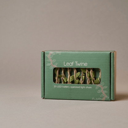 A green cardboard box labeled 'Leaf Twine' with a clear window showing twisted green and brown twine strands inside, photographed on a plain warm gray background.