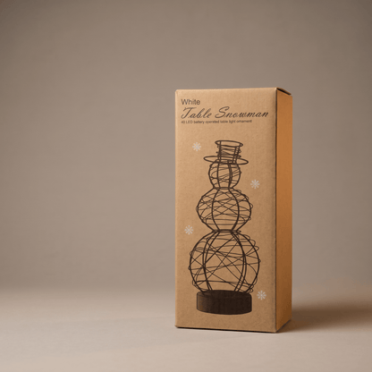 A tall rectangular kraft paper box standing upright on a neutral beige studio background. The box is printed with the words 'White Table Snowman' and a black line drawing of a snowman made of wire spheres on a base.