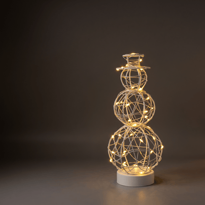 A snowman-shaped wire light sculpture with glowing warm white LED lights, standing on a round white base against a dark gray studio background.