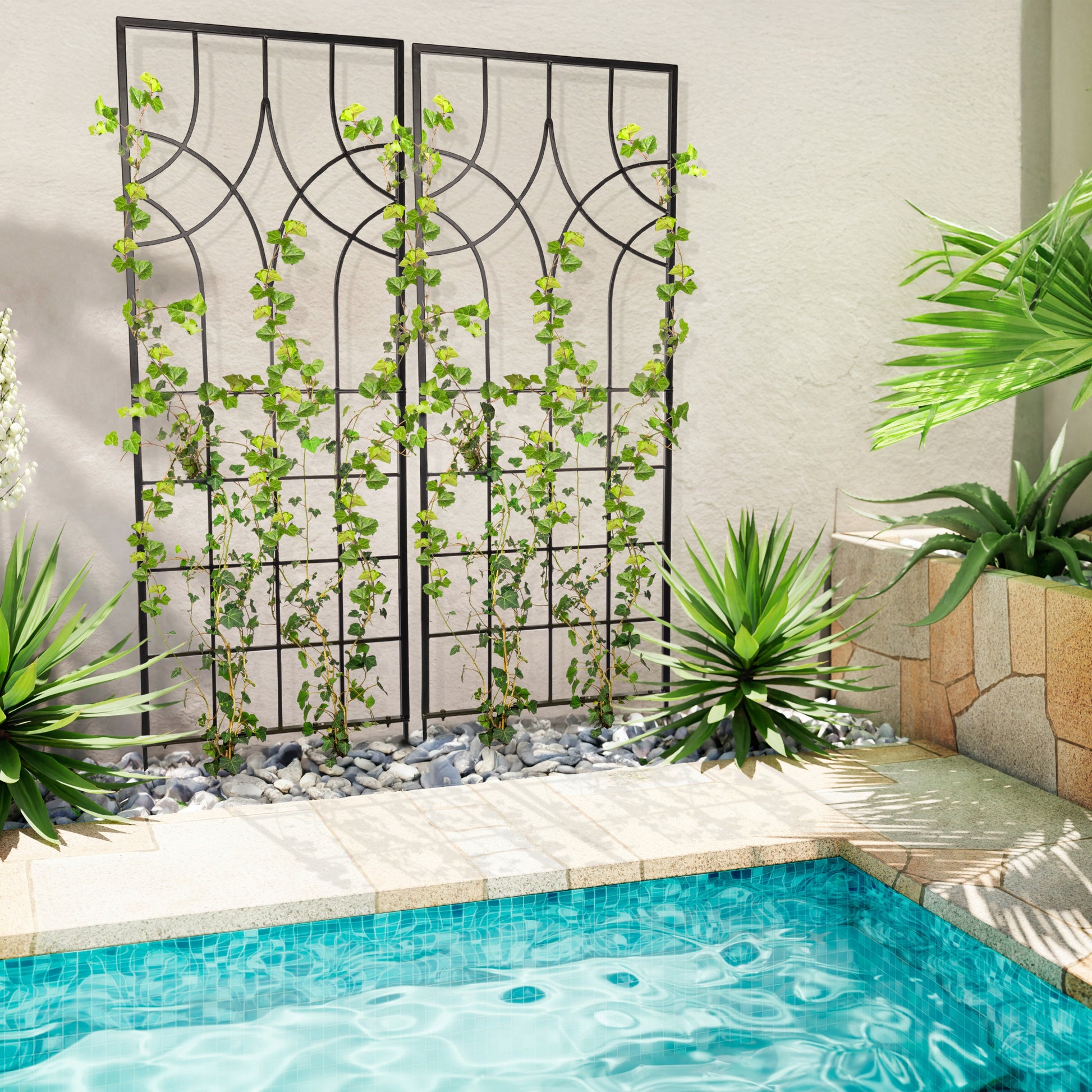 Two large black geometric iron garden trellises beside a pool with climbing plants, placed on a patio next to a wall.