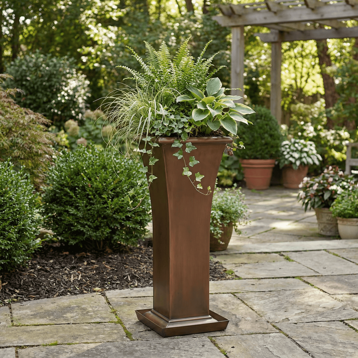 H Potter planter in copper antique finish on a stone patio with green plants and drip tray