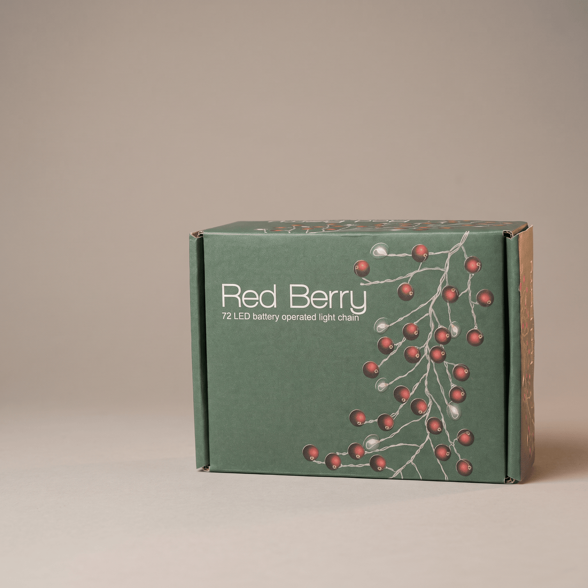 A green cardboard box for a 12 LED battery operated light chain, decorated with a red berry branch illustration and white text, set against a plain beige background.