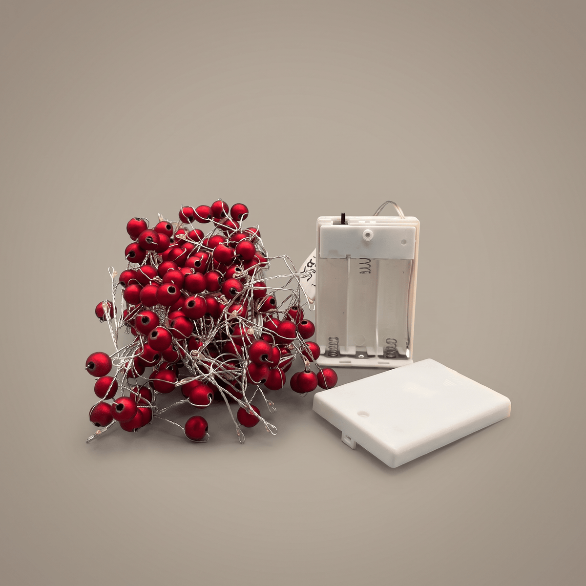h potter Red berry string lights with a white battery compartment and white battery cover, arranged on a plain taupe background.
