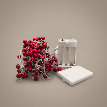 h potter Red berry string lights with a white battery compartment and white battery cover, arranged on a plain taupe background.