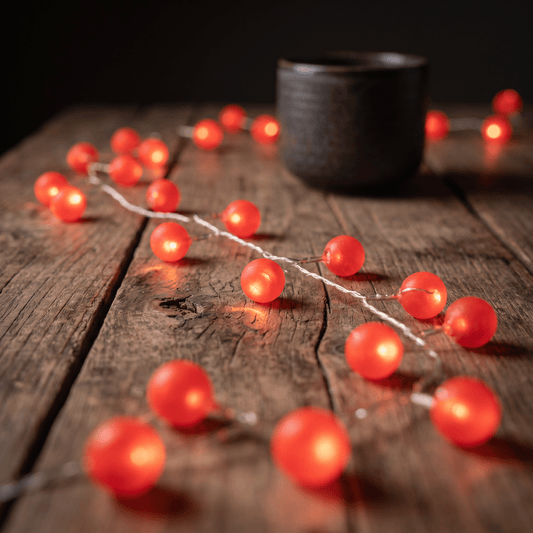 h potter LED string lights with glowing red round bulbs draped across a rustic wooden tabletop, with a dark ceramic cup blurred in the background.